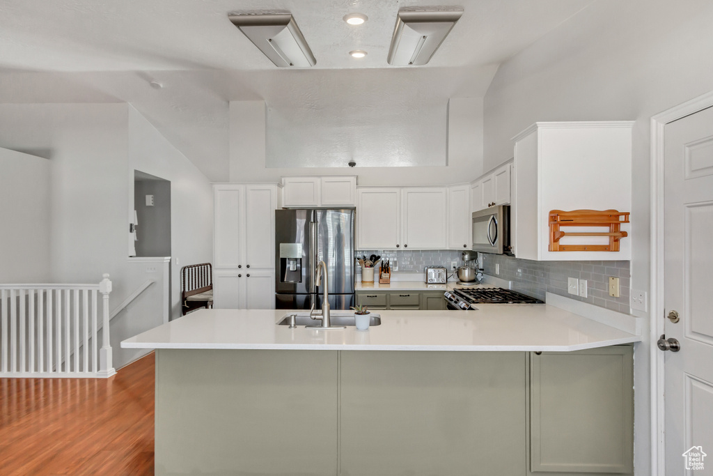 Kitchen with decorative backsplash, a peninsula, light countertops, a sink, and appliances with stainless steel finishes