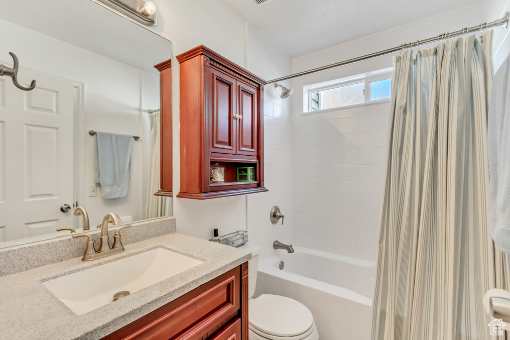 Bathroom featuring toilet, shower / bathtub combination with curtain, and vanity
