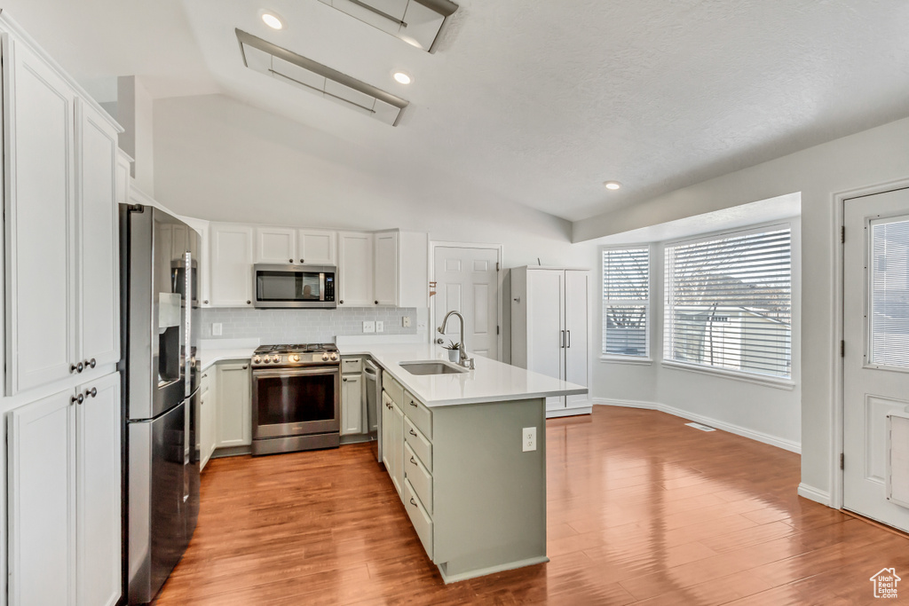 Kitchen featuring a sink, stainless steel appliances, a peninsula, decorative backsplash, and vaulted ceiling