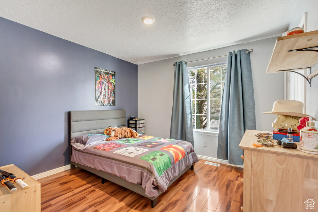 Bedroom featuring baseboards, a textured ceiling, visible vents, and wood finished floors