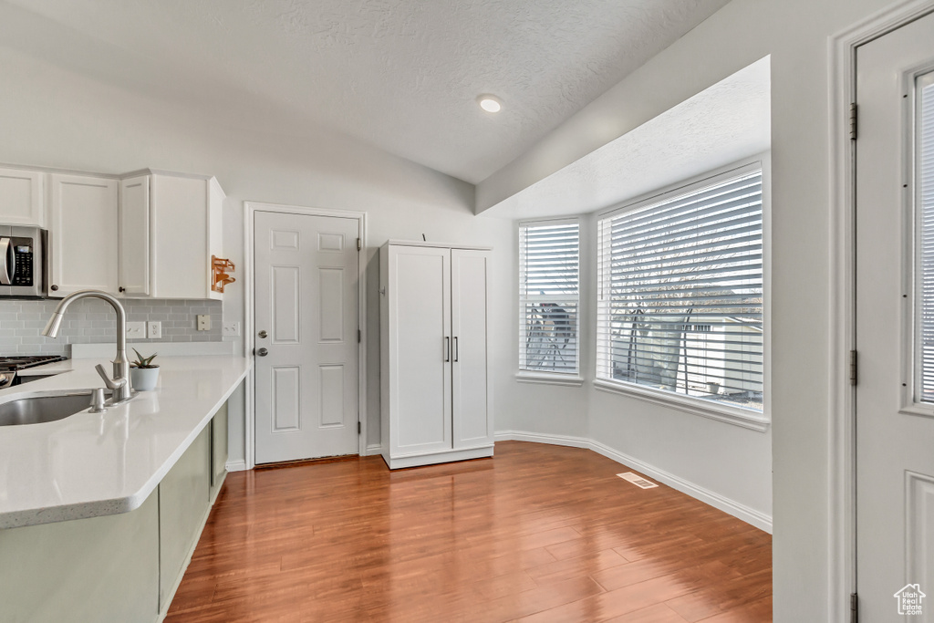 Kitchen with light countertops, stainless steel microwave, a sink, backsplash, and vaulted ceiling