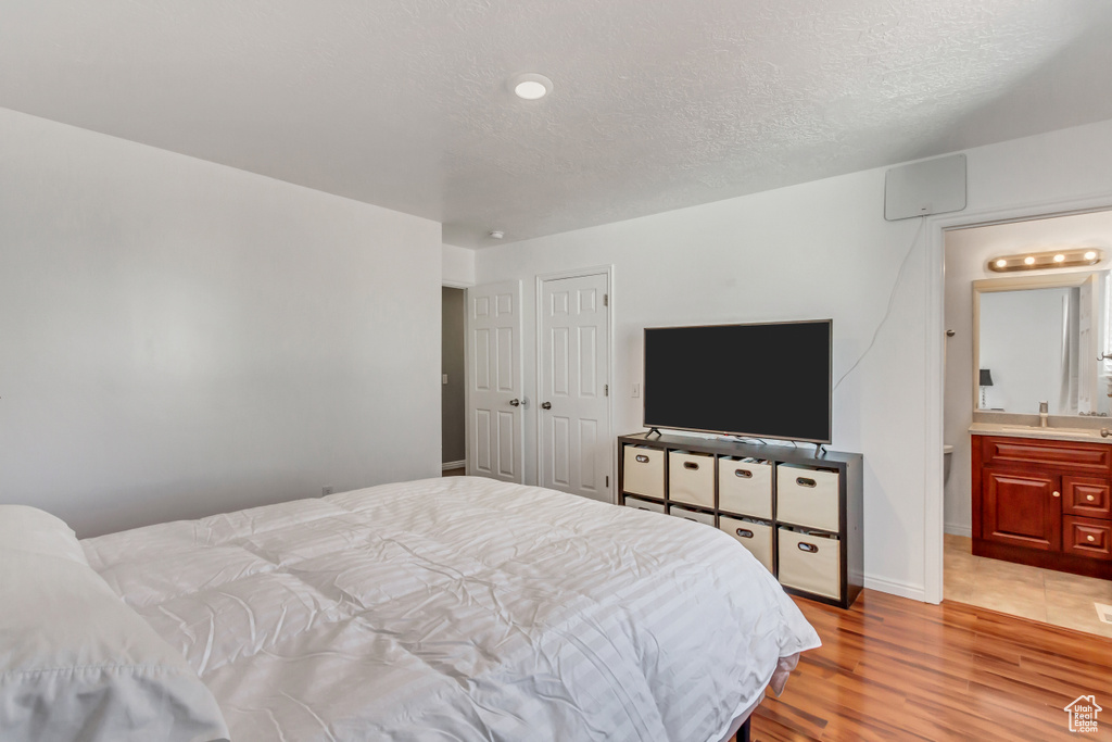 Bedroom with baseboards, a textured ceiling, light wood-style flooring, and ensuite bath