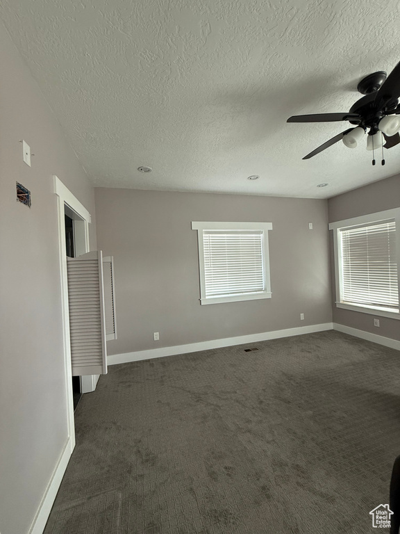 Spare room with a ceiling fan, a textured ceiling, and dark carpet