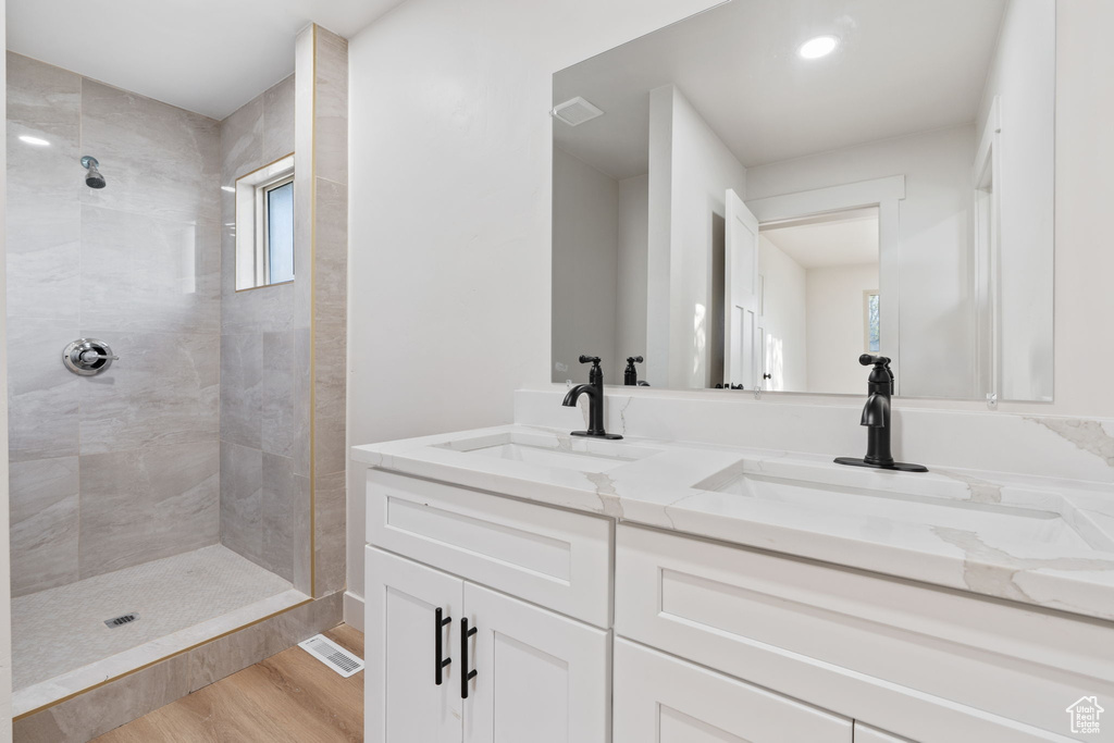 Full bathroom with a sink, double vanity, a tile shower, and wood finished floors