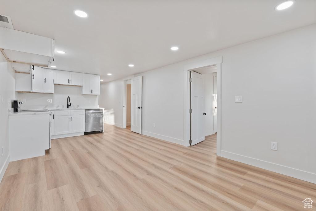 Kitchen featuring open shelves, stainless steel dishwasher, a sink, light wood finished floors, and white cabinetry