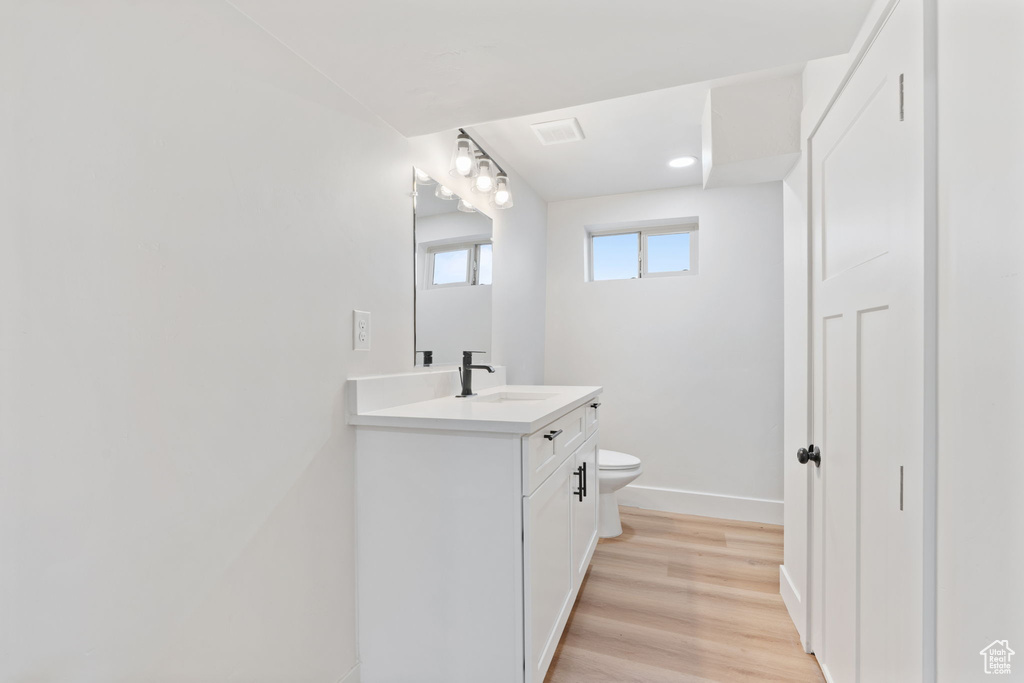 Half bath with visible vents, vanity, wood finished floors, toilet, and baseboards