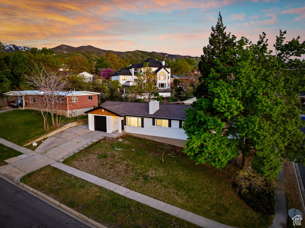 View of front facade with driveway, a chimney, a mountain view, a front lawn, and an attached garage