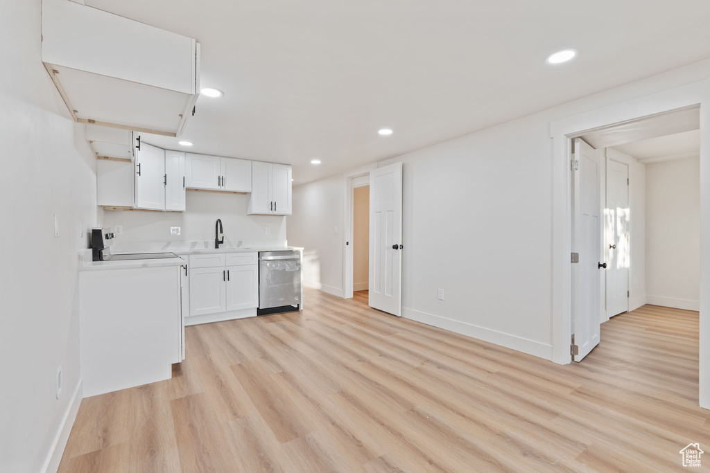 Kitchen with white cabinets, a sink, dishwasher, light countertops, and light wood-type flooring