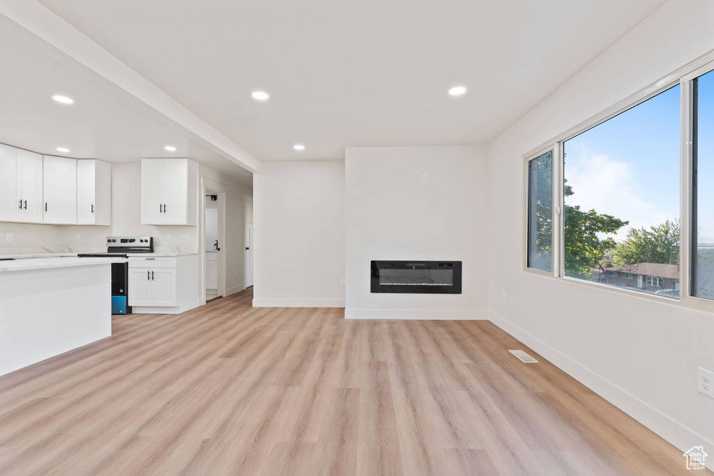 Unfurnished living room featuring recessed lighting, a glass covered fireplace, plenty of natural light, and light wood-style floors