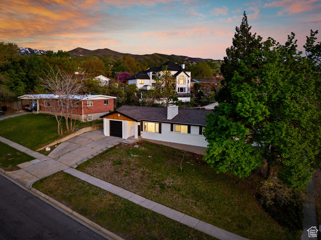 View of front of property with an attached garage, aphalt driveway, a mountain view, a chimney, and a lawn