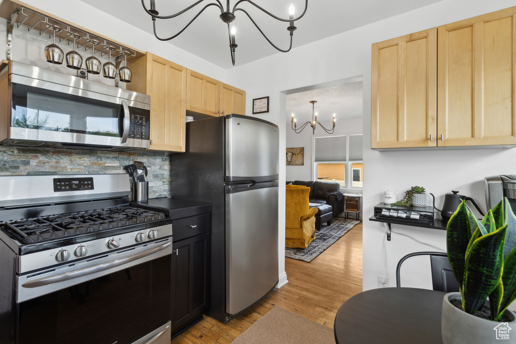 Kitchen featuring light brown cabinetry, stainless steel appliances, light wood-type flooring, and a chandelier