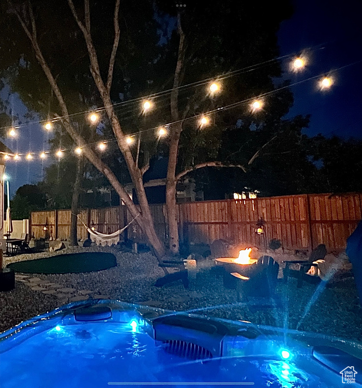 Pool at night with a hot tub, a fire pit, and a fenced backyard
