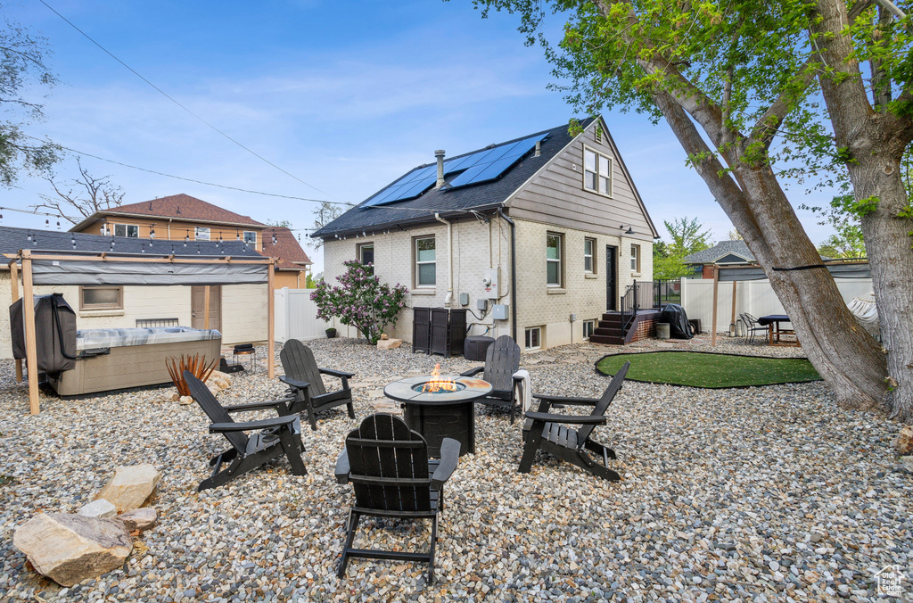 Back of property with a fire pit, a patio, a fenced backyard, brick siding, and solar panels