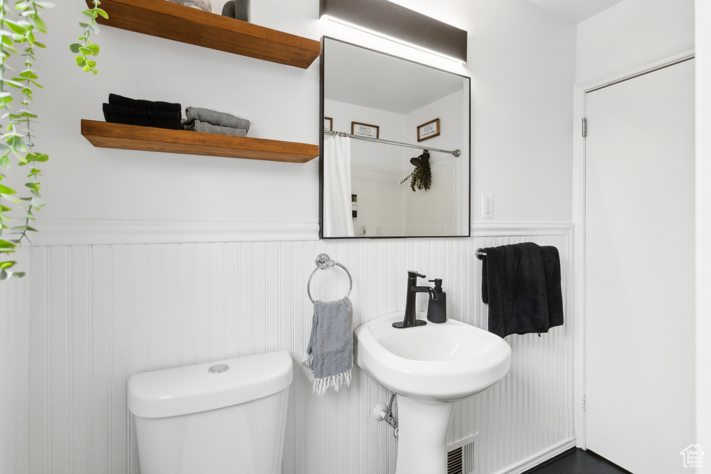 Bathroom featuring a sink, a wainscoted wall, toilet, and a shower with shower curtain