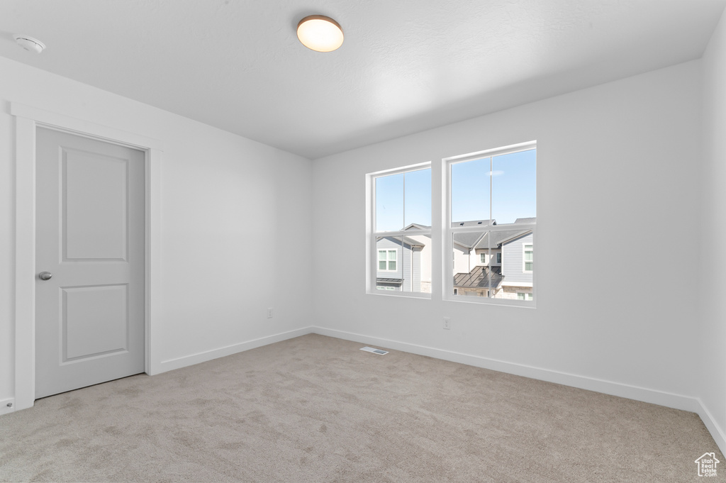 Empty room with baseboards, visible vents, and light carpet