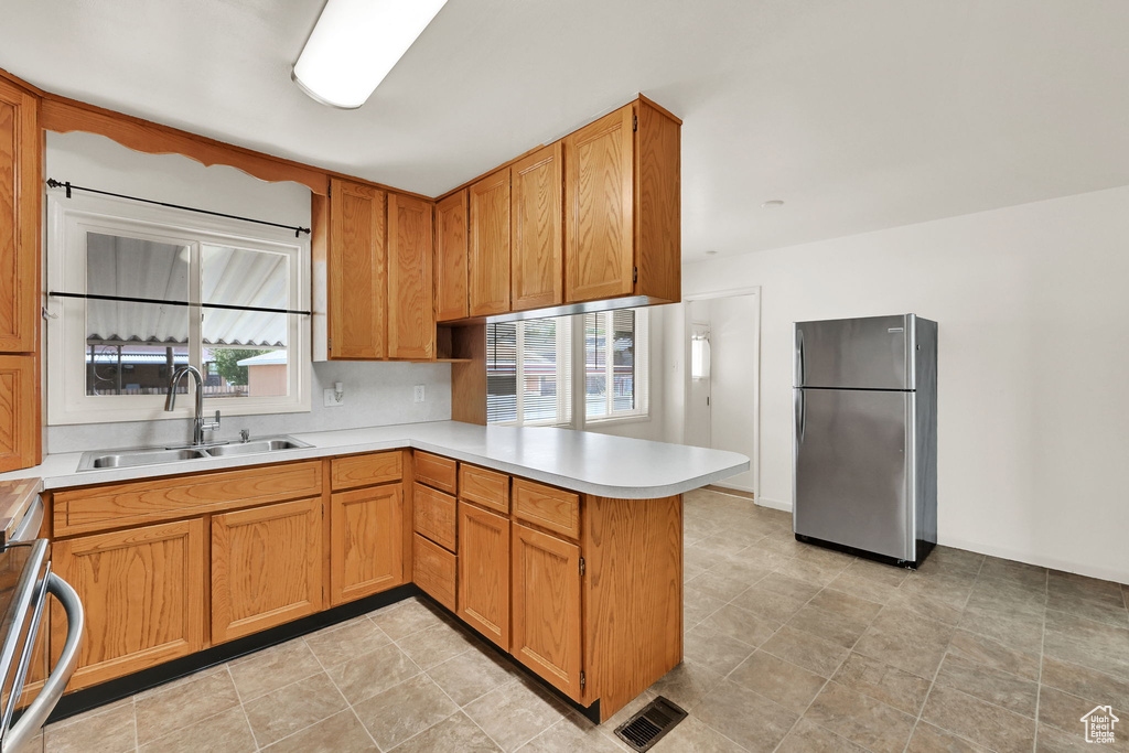 Kitchen featuring visible vents, a sink, light countertops, freestanding refrigerator, and a peninsula