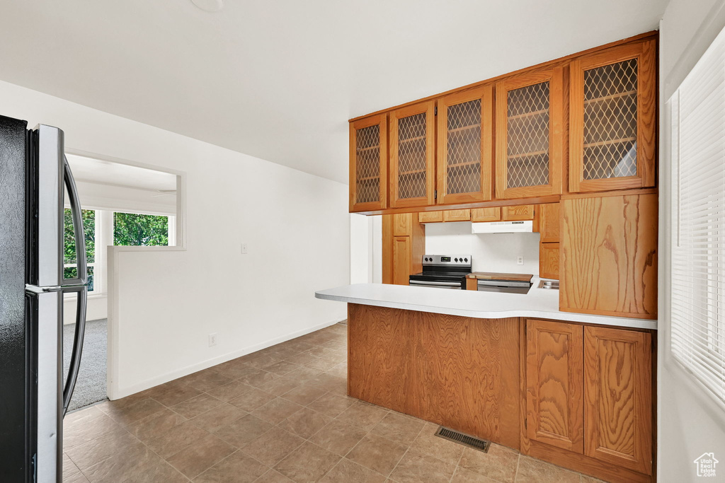 Kitchen with visible vents, freestanding refrigerator, a peninsula, under cabinet range hood, and stainless steel range with electric cooktop