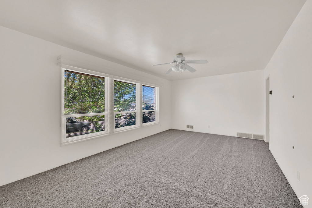 Carpeted empty room featuring visible vents and ceiling fan