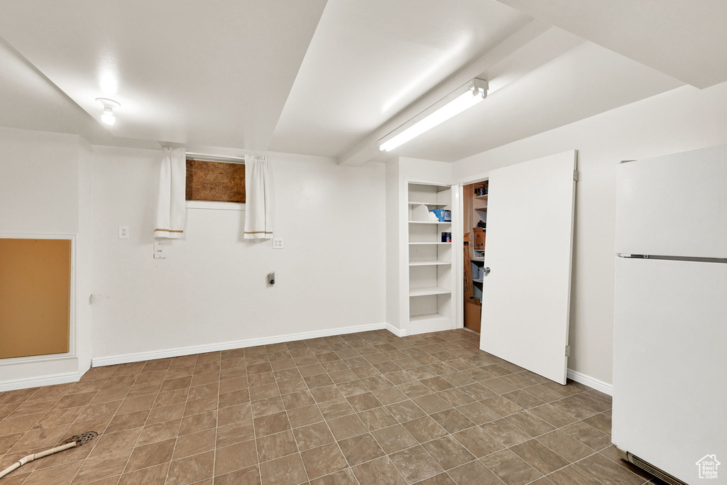 Finished below grade area featuring baseboards, freestanding refrigerator, and built in shelves