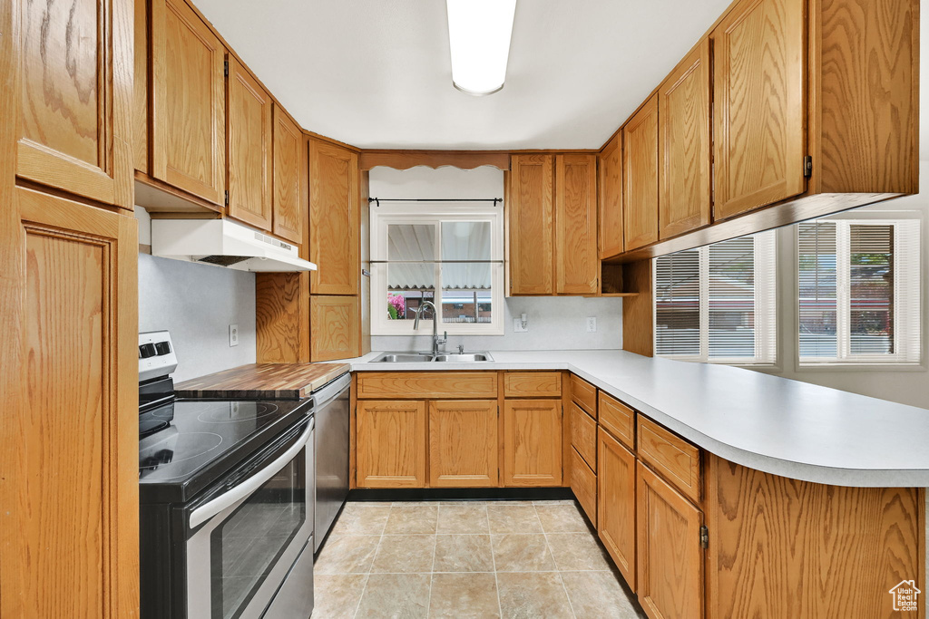 Kitchen with a peninsula, light countertops, under cabinet range hood, a sink, and appliances with stainless steel finishes