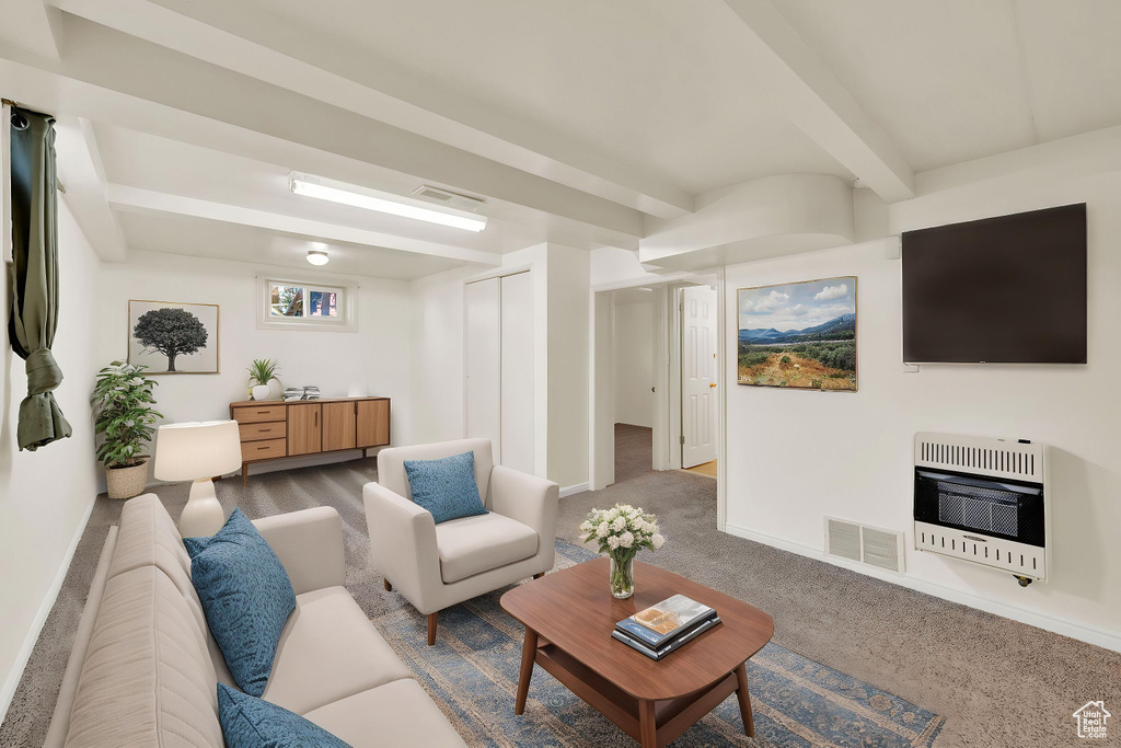 Carpeted living room with heating unit, baseboards, beam ceiling, and visible vents