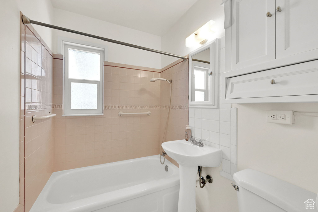 Bathroom featuring toilet, shower / washtub combination, a wealth of natural light, and tile walls
