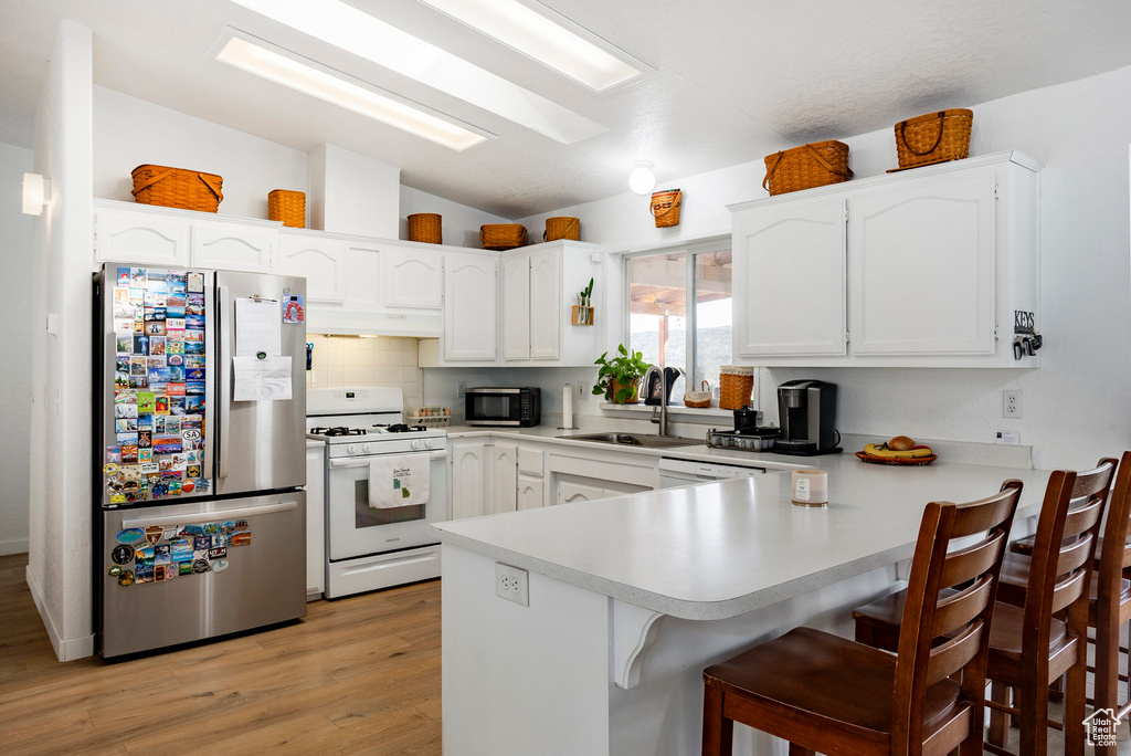 Kitchen with vaulted ceiling, a sink, a peninsula, under cabinet range hood, and stainless steel appliances
