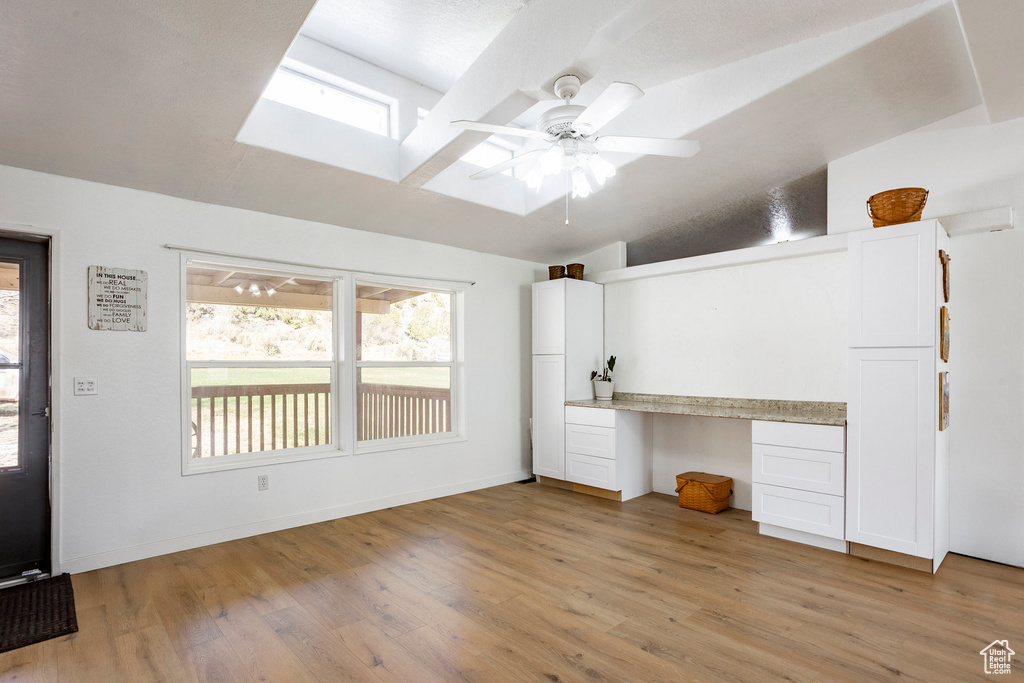 Interior space featuring light wood finished floors, built in study area, a ceiling fan, baseboards, and a skylight