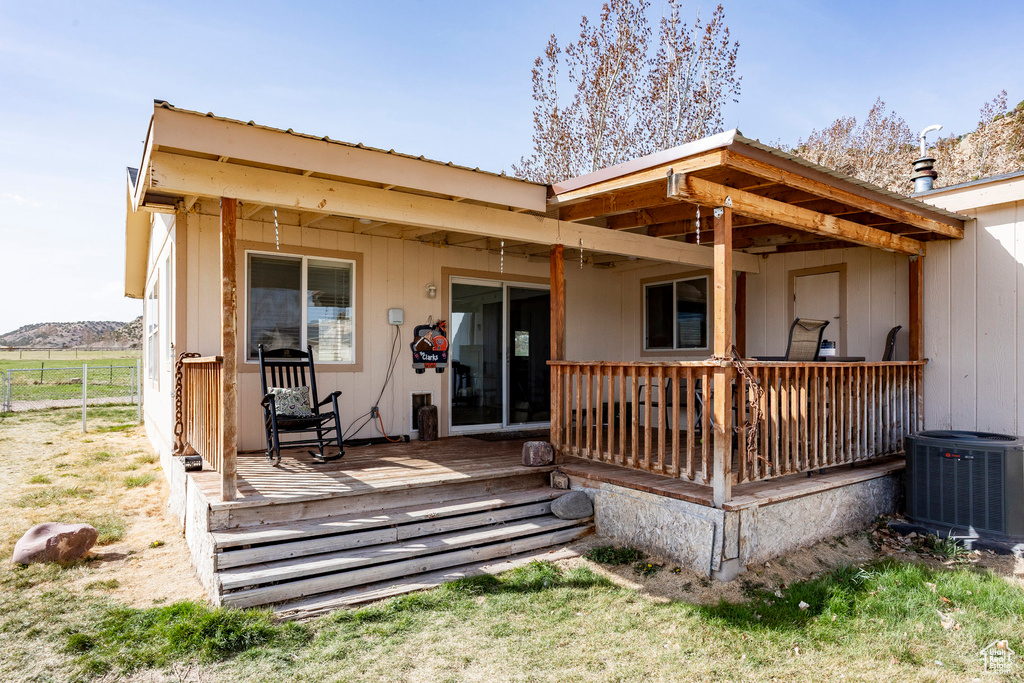 Rear view of house with a deck, cooling unit, and fence