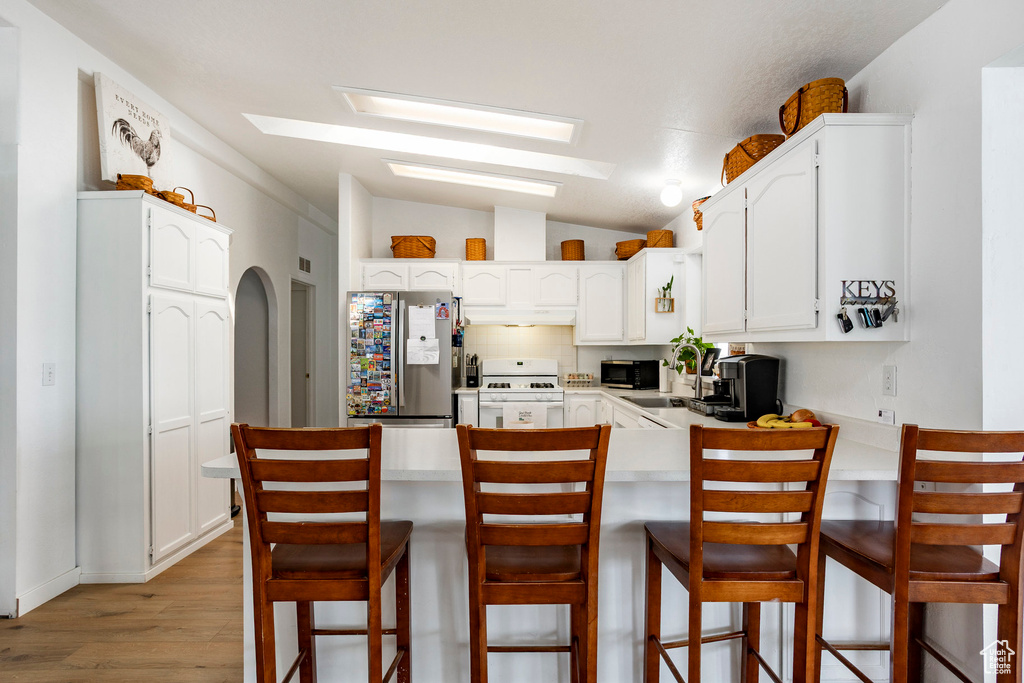 Kitchen featuring white cabinets, light wood-style floors, freestanding refrigerator, a peninsula, and white range with gas stovetop