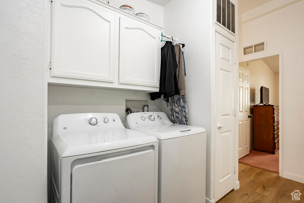 Clothes washing area with visible vents, light wood-style flooring, cabinet space, and washer and dryer