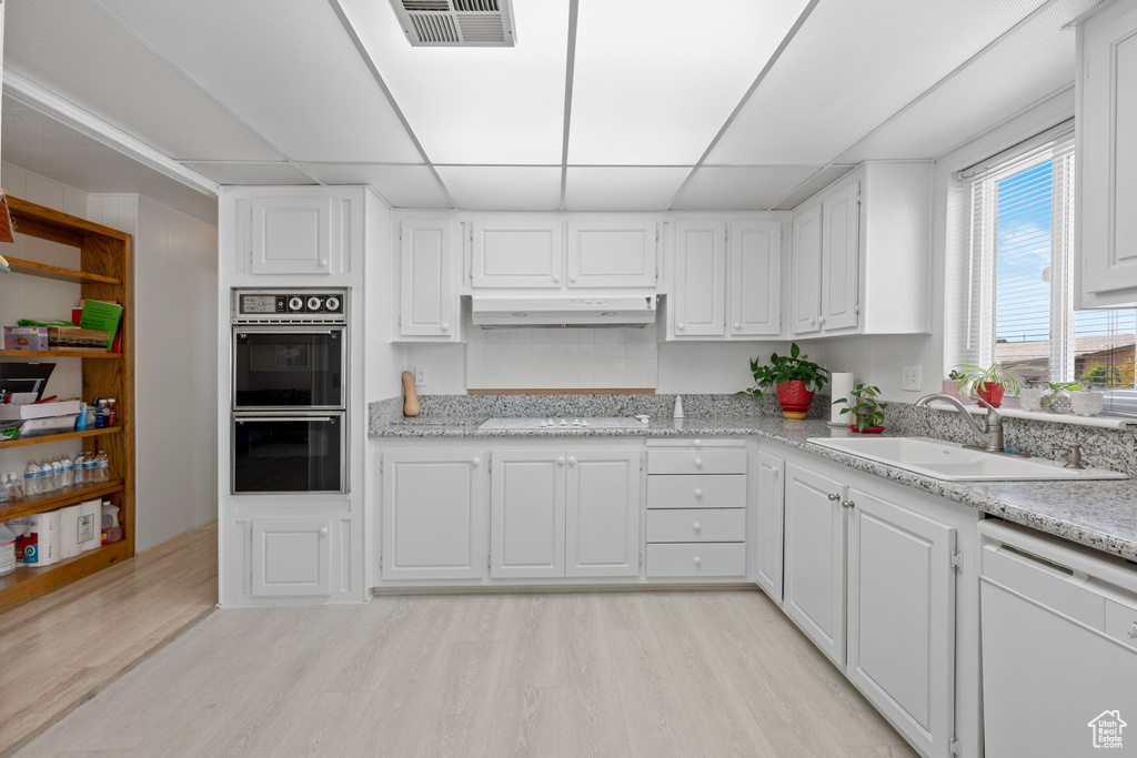 Kitchen with visible vents, white appliances, light wood-style floors, under cabinet range hood, and a sink