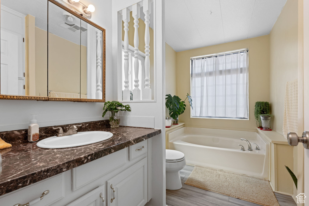 Bathroom featuring a bath, vanity, toilet, and wood finished floors