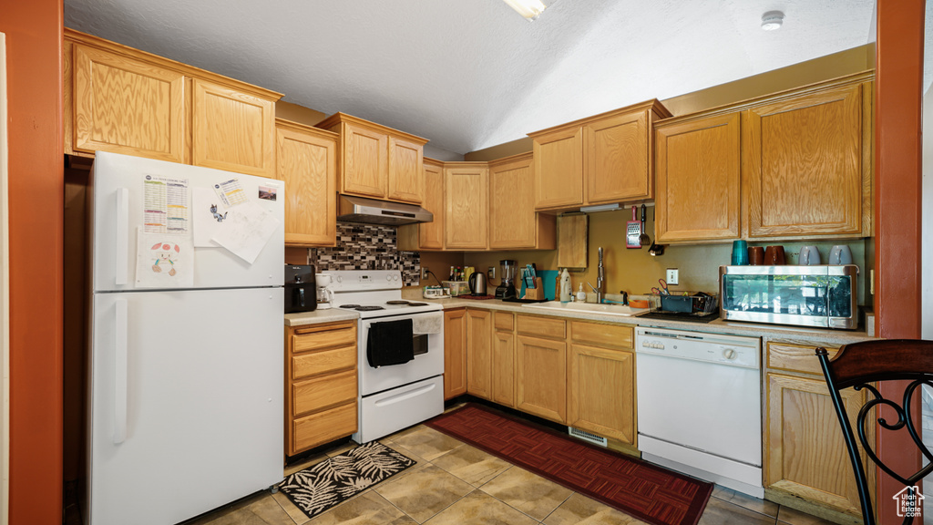 Kitchen with white appliances, under cabinet range hood, a sink, lofted ceiling, and light countertops