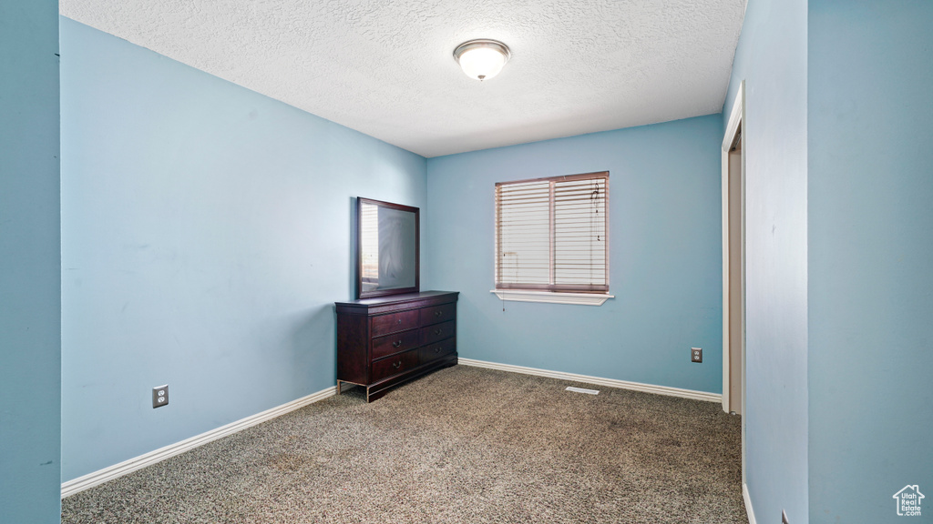 Unfurnished bedroom with a textured ceiling, carpet flooring, and baseboards