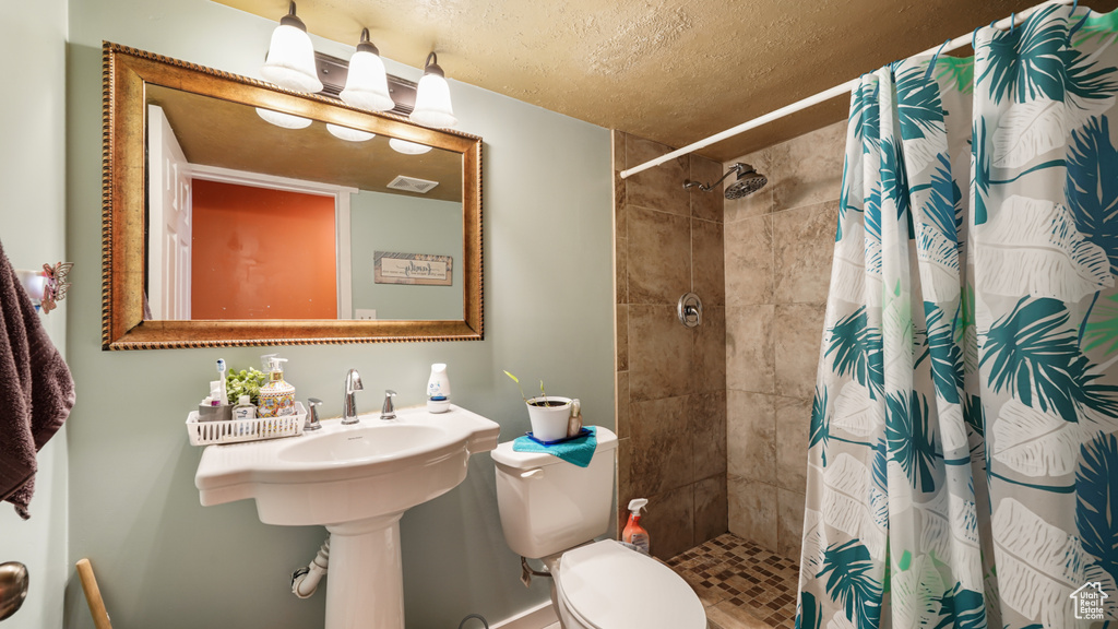 Full bath featuring toilet, tiled shower, and a textured ceiling