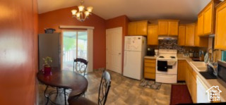 Kitchen featuring exhaust hood, a notable chandelier, white appliances, light countertops, and vaulted ceiling