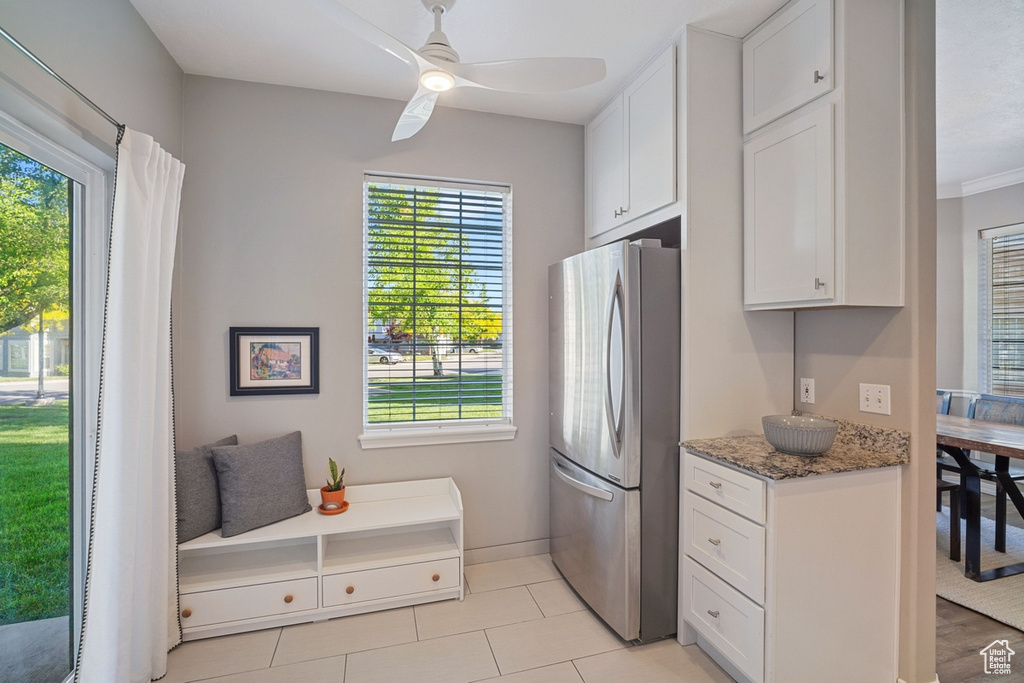 Kitchen with white cabinets, light stone counters, freestanding refrigerator, a ceiling fan, and baseboards