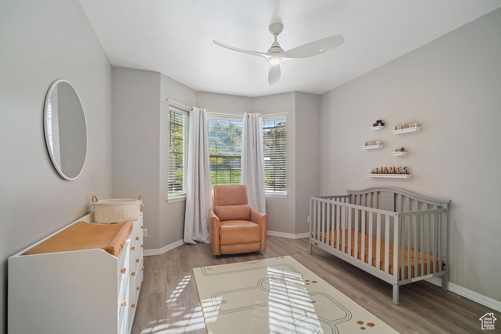 Bedroom featuring a crib, baseboards, a ceiling fan, and wood finished floors