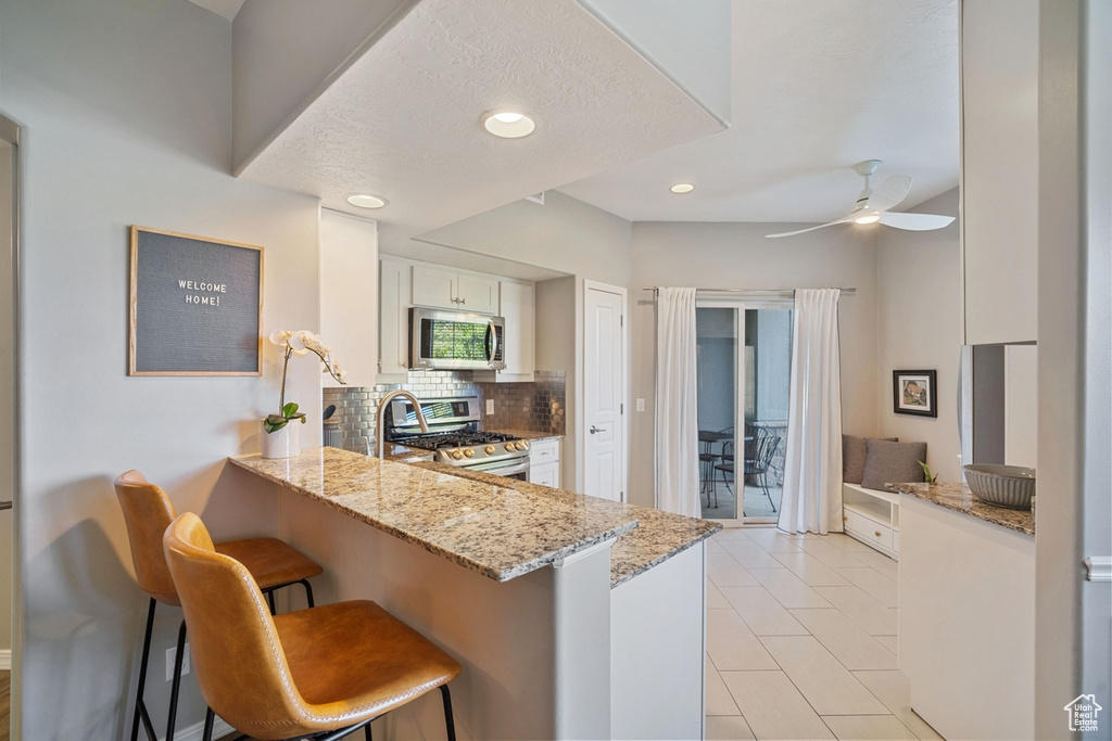Kitchen with stainless steel appliances, white cabinetry, a peninsula, a kitchen bar, and backsplash
