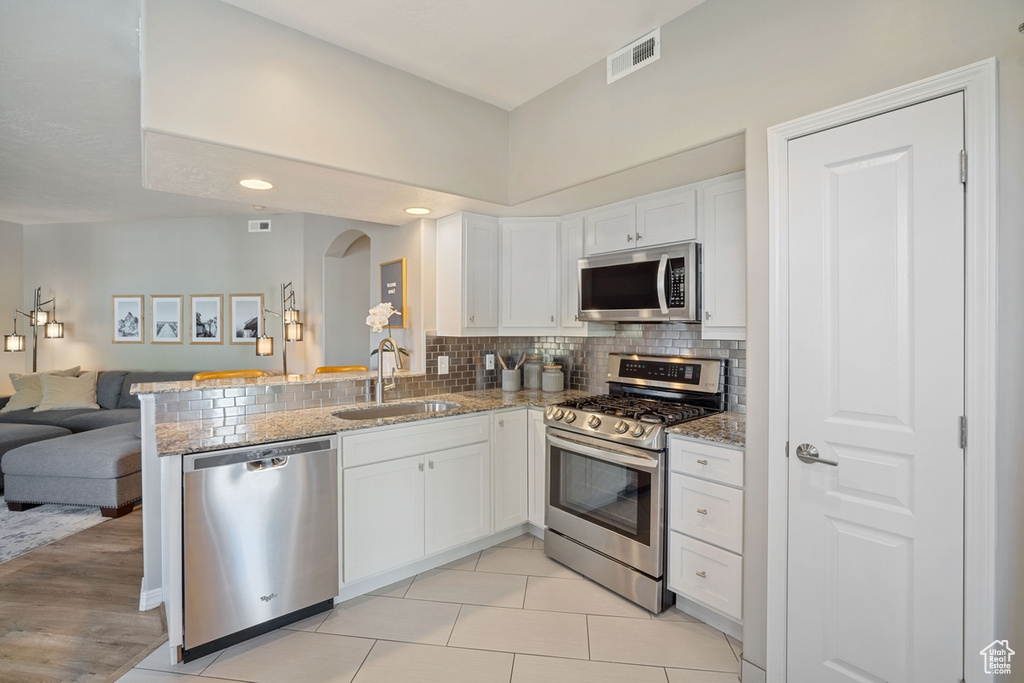 Kitchen featuring white cabinets, appliances with stainless steel finishes, a sink, arched walkways, and open floor plan
