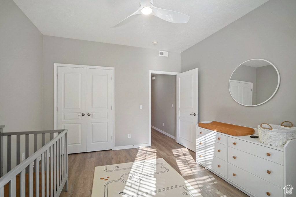 Bedroom with ceiling fan, a crib, light wood-style flooring, baseboards, and a closet