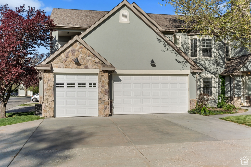 View of front of property featuring stone siding, roof with shingles, stucco siding, an attached garage, and driveway
