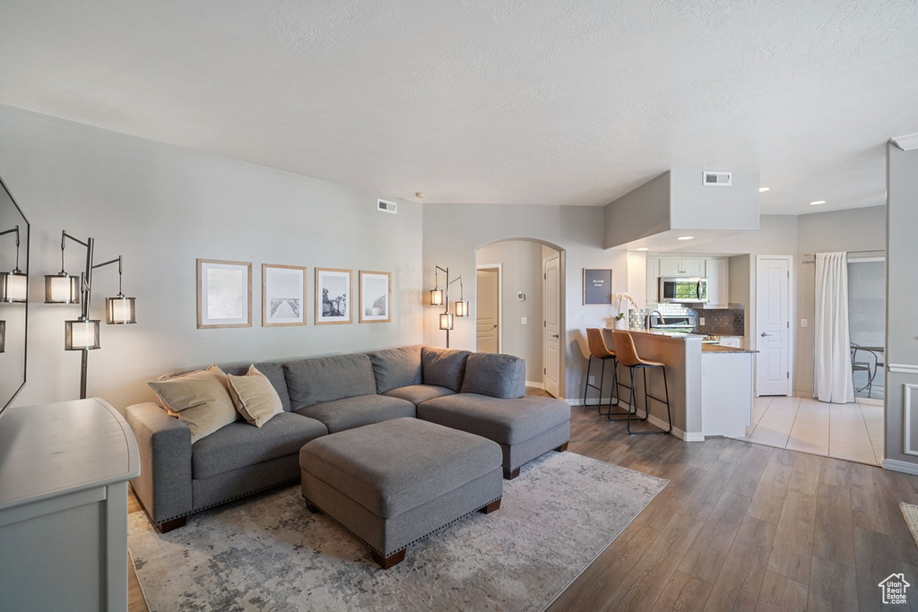Living room with visible vents, light wood-style floors, baseboards, recessed lighting, and arched walkways