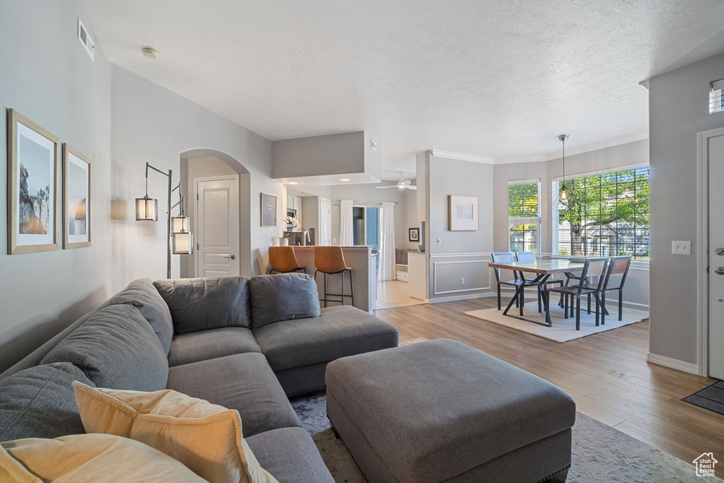 Living room with ceiling fan, visible vents, arched walkways, baseboards, and light wood finished floors