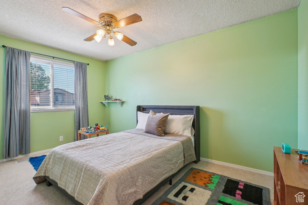 Carpeted bedroom featuring baseboards, ceiling fan, and a textured ceiling