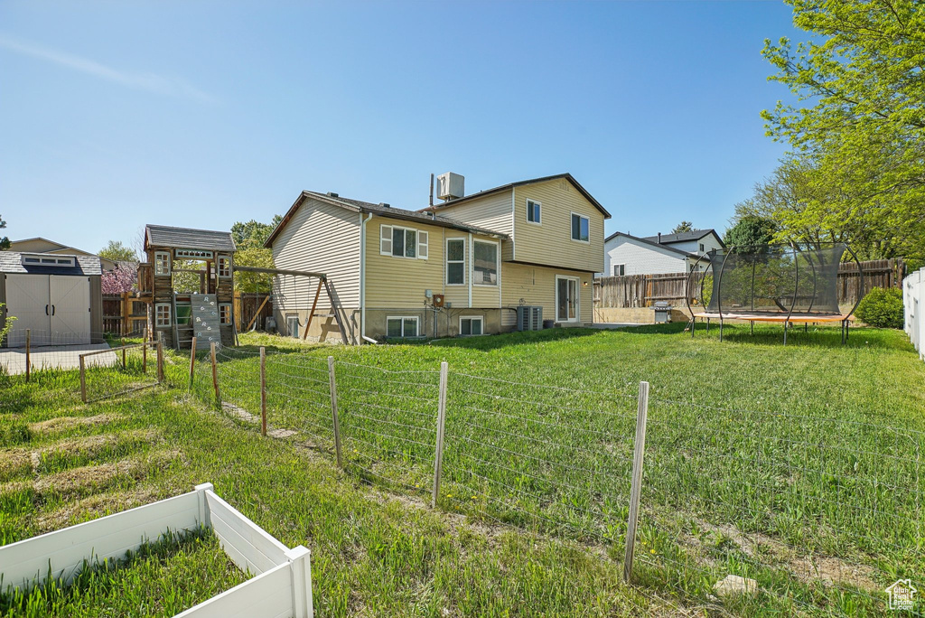 Back of property featuring a trampoline, an outbuilding, a fenced backyard, a shed, and a yard