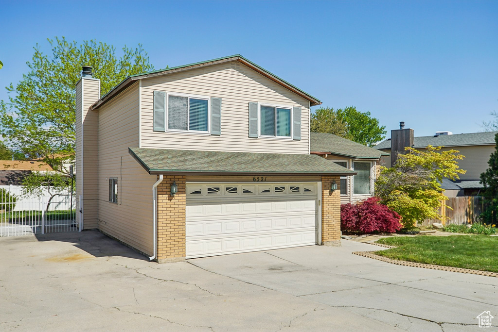 Split level home featuring concrete driveway, brick siding, an attached garage, and fence