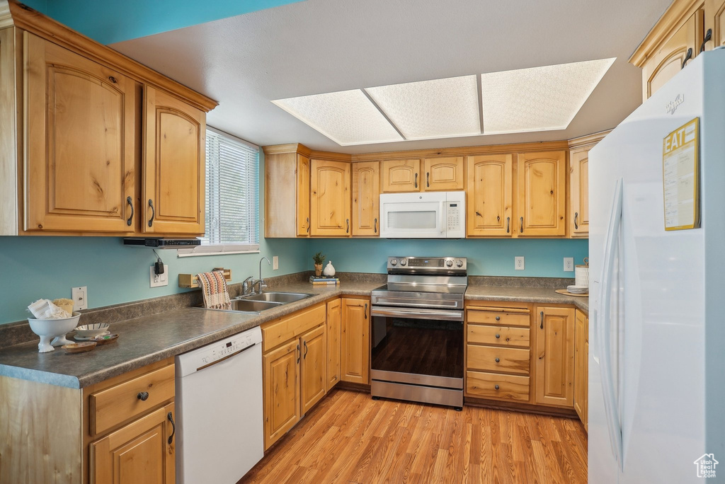 Kitchen with a sink, dark countertops, light wood-type flooring, and white appliances