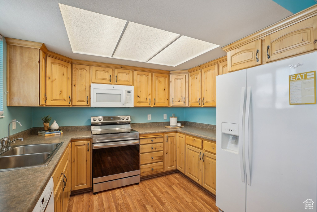 Kitchen with white appliances, dark countertops, a sink, and light wood-style floors